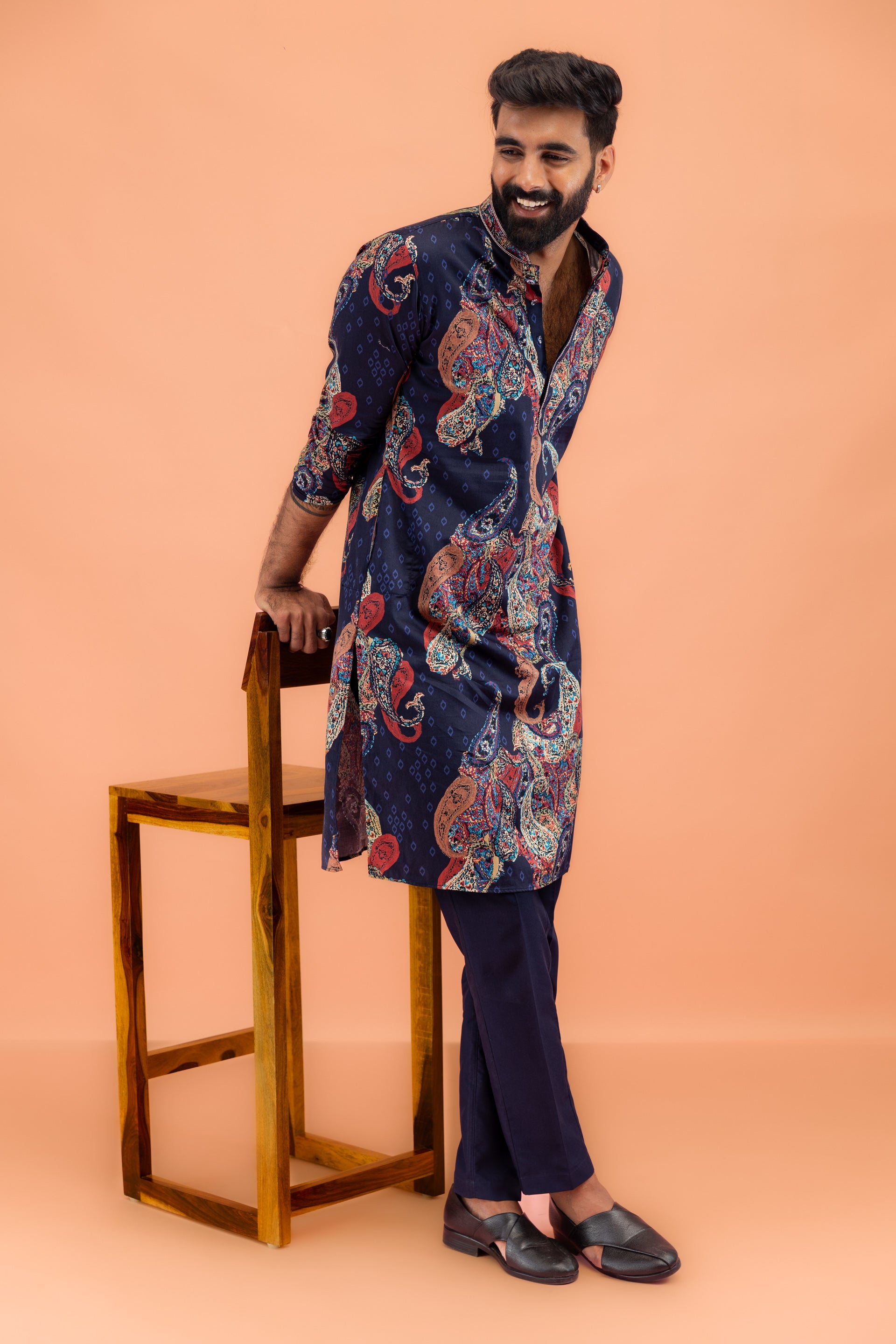 The man leans over a chair and poses in Kisah's Navy Blue Kurta Trouser Set